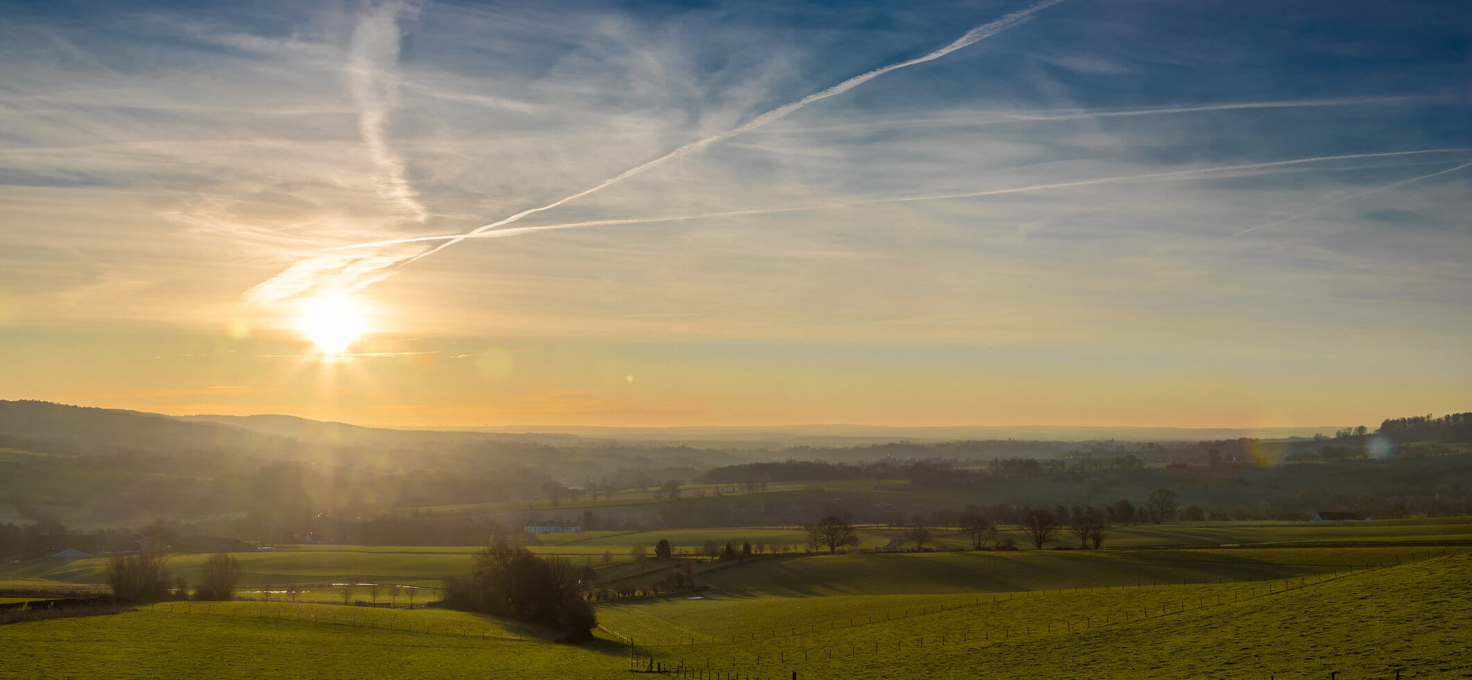 A cold sunrise over the rolling hills in the south of the Netherlands, giving a winter feeling with the first beams of the sun over the green meadows and hills
